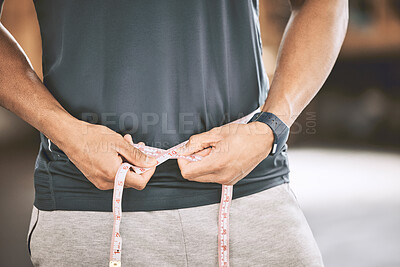 Hands of a bodybuilder measuring his waist. Fit trainer using tape measure in the gym. Active athlete tracking his body weight and diet. Sporty man measuring his size in the gym.