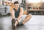 Portrait of strong trainer stretching. Young athlete sitting on the floor to warmup. Hispanic bodybuilder stretching his leg. Happy, strong fitness man stretching before workout class.