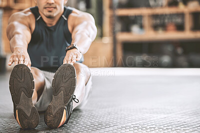 Fit man stretching his leg. Bodybuilding sitting on gym floor for a warmup. Athletic, muscular trainer stretching before exercise class. Sporty man preparing for a workout routine