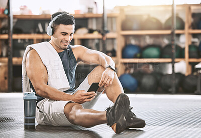 Muscular trainer taking a break from exercise. Young bodybuilder listening to music in headphones. Happy athlete using his smartphone in the gym. Strong, fit man relaxing after a workout