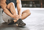 Athlete touching his sprained ankle. Closeup of hands of bodybuilder sitting on the gym floor. Sporty trainer taking a break after a workout class. Strong trainer with an ankle injury