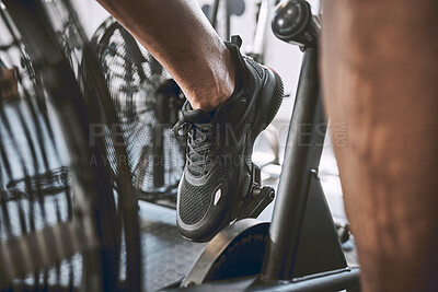 Foot of a fit man cycling in the gym. Trainer cycling in sport shoes in the gym. Bodybuilder riding a gym bike cropped. Wear the right shoes when exercising at the gym. Building strong legs on a bike