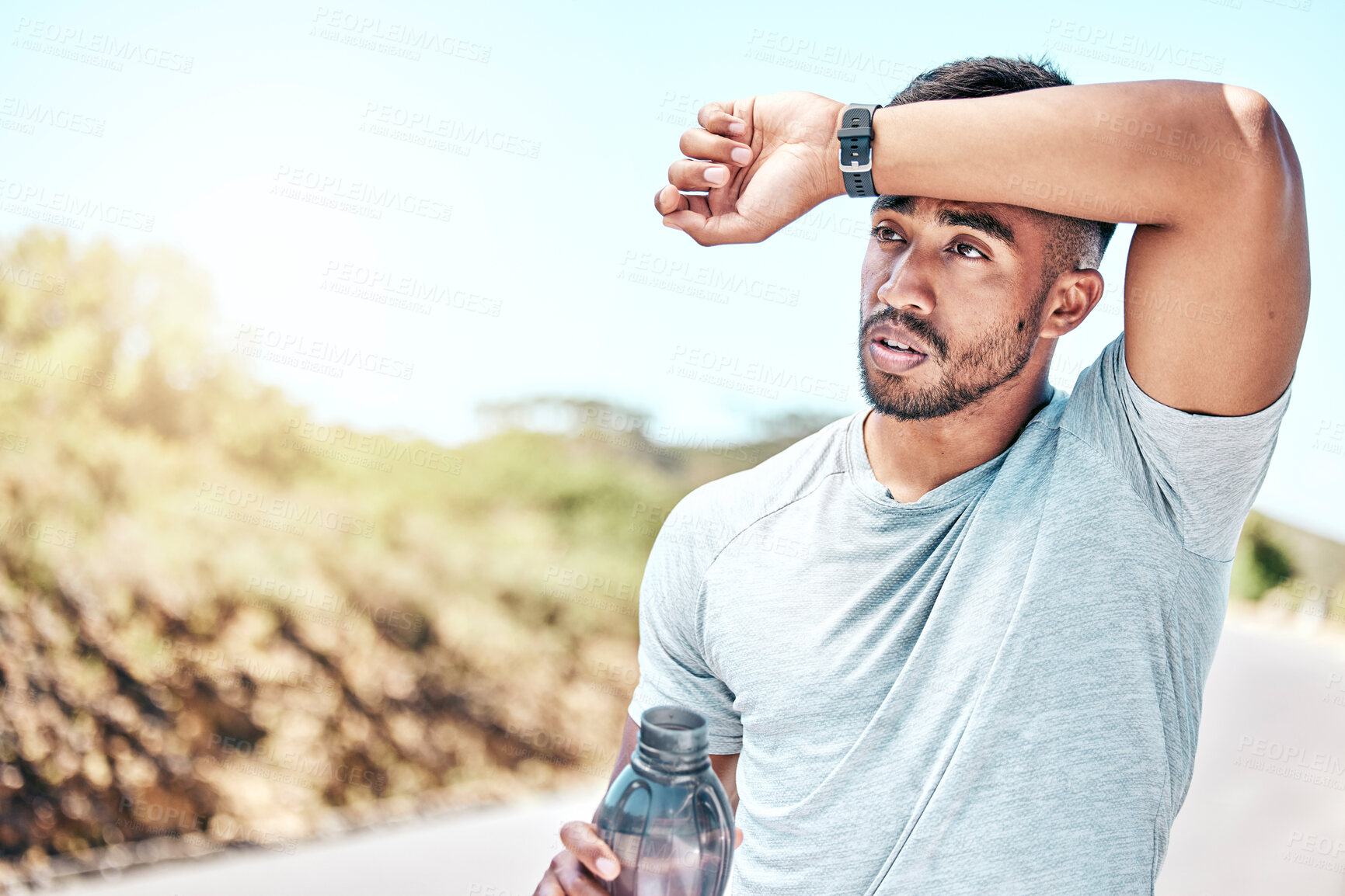 Buy stock photo Fit young mixed race man looking tired and drinking from a water bottle while exercising outdoors. Handsome hispanic male taking a sip during a break from his cardio and endurance workout outside