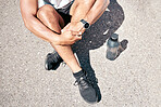 Above sporty young man sitting on a road with his water bottle during a break. Male athlete wearing a smart watch and resting outside during a workout. Staying hydrated while exercising for fitness