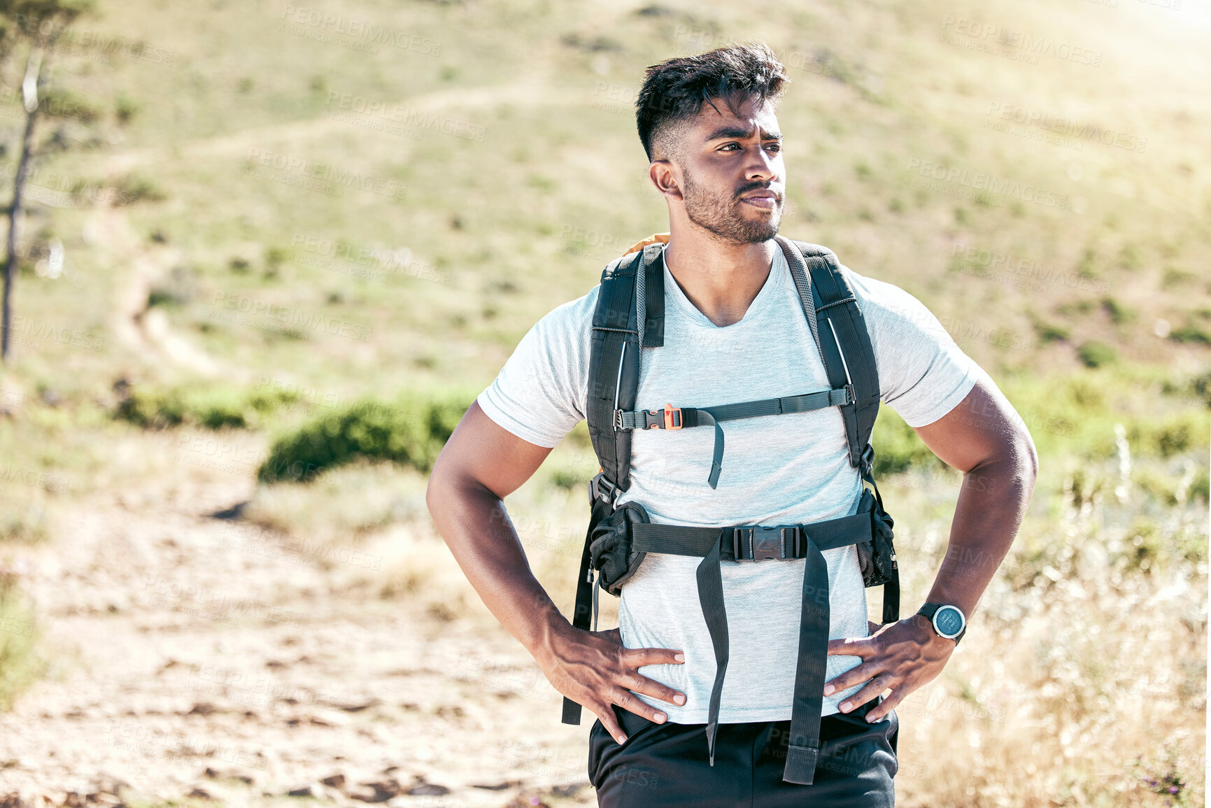 Buy stock photo Athletic young mixed race man wearing a backpack taking a break during a hike. Fit handsome hispanic man standing outside and looking at the view while hiking outside in nature. An outdoor workout