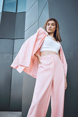 Portrait of a young trendy and confident mixed race woman looking stylish while posing and chilling time in the city. Fashionable hispanic woman wearing pink clothes and standing outside downtown