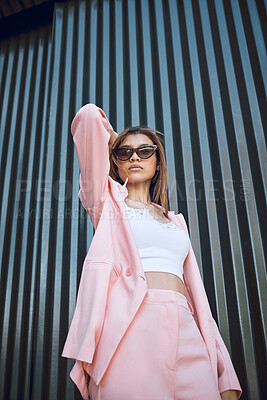 A young trendy and confident mixed race woman looking stylish while posing and spending time in the city. Fashionable hispanic woman wearing pink clothes and sunglasses