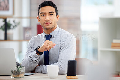 Buy stock photo Young serious mixed race businessman working on a laptop alone in an office at work. One confident hispanic businessperson sitting at a desk at work