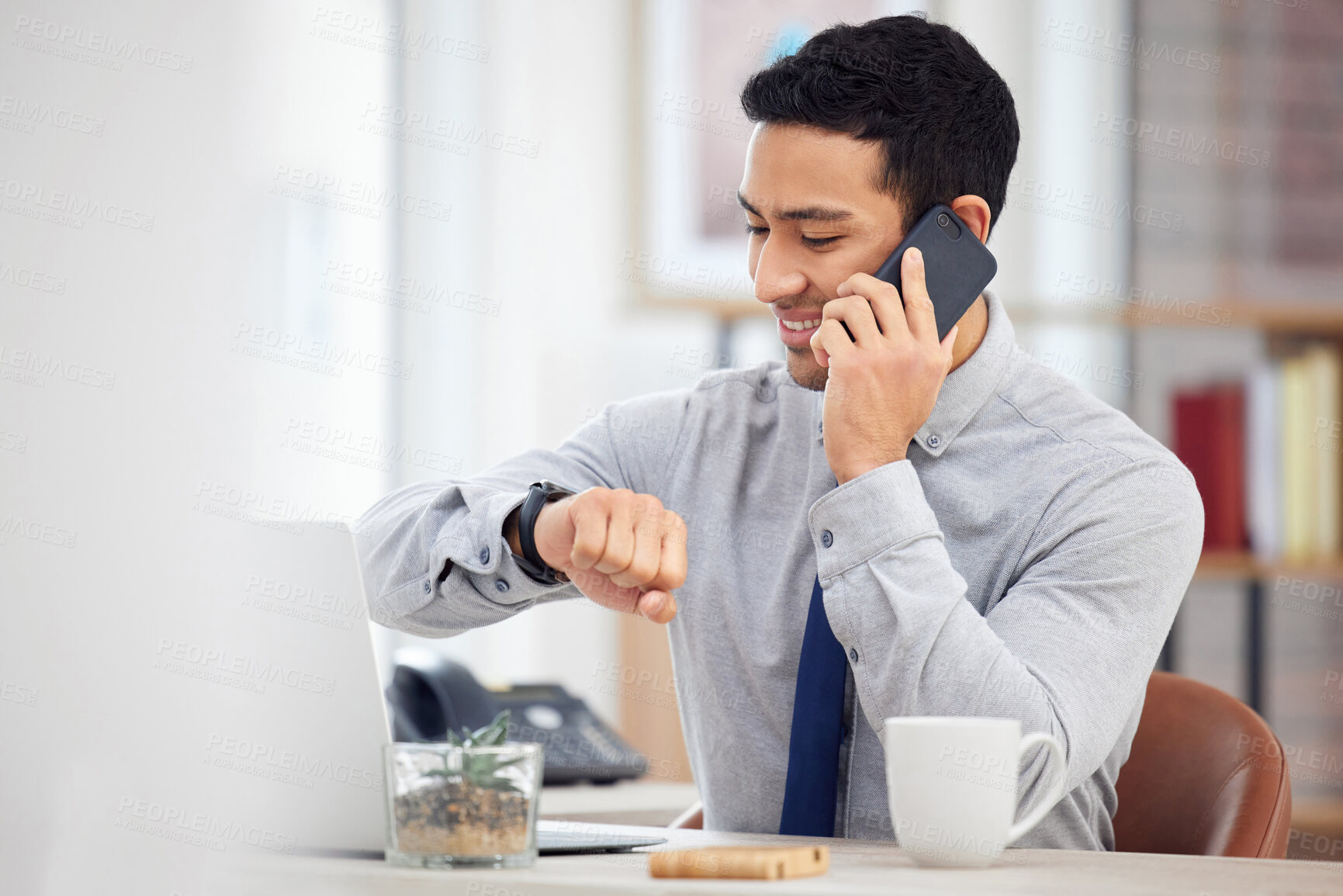 Buy stock photo Mixed race businessman on a call using a phone and checking the time on his watch while sitting in an office at work. Hispanic male businessperson talking on the phone while looking the time at work