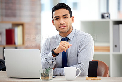 Buy stock photo Young serious mixed race businessman working on a laptop alone in an office at work. One focused confident hispanic businessperson sitting at a desk at work