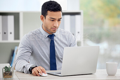 Young serious mixed race businessman working on a laptop alone in an office at work. One focused hispanic male boss sitting at a desk at work
