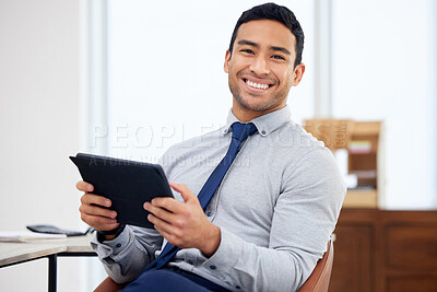 Buy stock photo Young happy mixed race businessman holding and using a digital tablet sitting in an office at work. Hispanic male businessperson smiling while working on a digital tablet at work