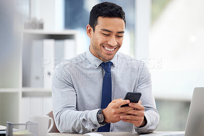 Buy stock photo Young content mixed race businessman holding and using a phone sitting in an office at work. One hispanic male businessperson smiling while typing a text on a cellphone sitting at a desk