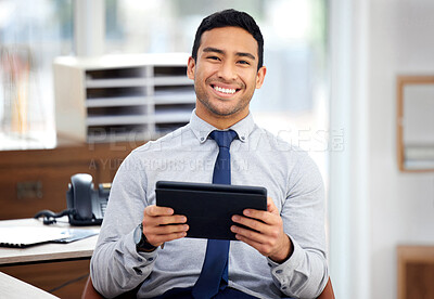 Buy stock photo Young happy mixed race businessman holding and using a digital tablet sitting in an office at work. Content hispanic male businessperson smiling while using social media on a digital tablet at work