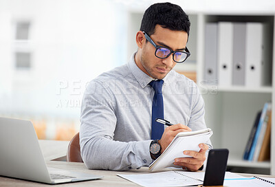 Young focused mixed race businessman writing In a notebook alone in an office at work. One hispanic male businessperson taking notes in a diary sitting at a desk in an office