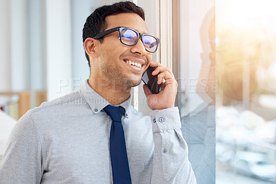 Young content mixed race businessman on a call using a phone and standing in an office at work. One hispanic male businessperson smiling while talking on the phone standing and thinking at a window in an office