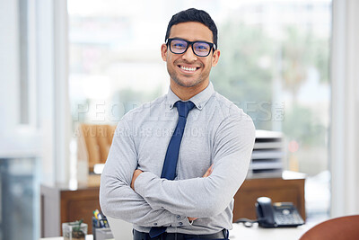 Young happy mixed race businessman standing with his arms crossed alone in an office at work. Headshot of a confident hispanic businessperson wearing glasses while standing at work