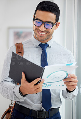 Buy stock photo Happy  mixed race businessman reading a report alone in an office at work. Hispanic male businessperson wearing glasses smiling while looking at a document and standing in an office