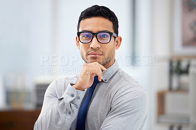 Young serious mixed race businessman standing alone in an office at work. Face of a confident hispanic businessperson wearing glasses while standing at work