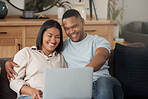 Attractive young mixed race couple relaxing on the sofa and using a laptop. Smiling African American couple watching movies while being affectionate and bonding at home together