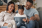 A happy mixed race family of three relaxing on the sofa at home. Loving black family being affectionate on the sofa while using a digital tablet and streaming. Young couple bonding with their daughter and watching movies at home