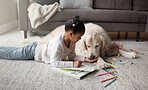 Sweet little mixed race child doing her homework while lying on the living room carpet with her puppy. Child colouring while bonding with her emotional  support rescue dog