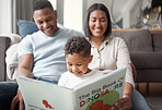 A happy mixed race family of three relaxing on the lounge floor  and reading a story book at home. Loving black family being affectionate on a carpet. Young couple bonding with their son at home