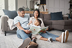 A happy mixed race family of three relaxing on the lounge floor  and reading a story book at home. Loving black family being affectionate on a carpet. Young couple bonding with their son at home