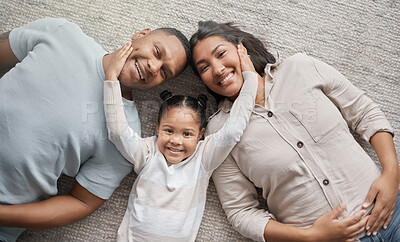Portrait of a mixed race family of three relaxing on the lounge floor at home. Loving black family being affectionate on a carpet. Young couple bonding with their daughter at home