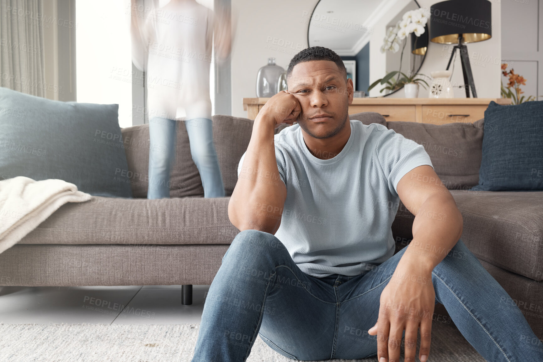 Buy stock photo A black single parent looking depressed while his son has fun jumping on the sofa next to home. Worried young father looking stressed at home