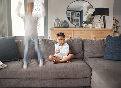 Buy stock photo Two young mixed race siblings showing their different personalities while sitting on a sofa at home. Cute child looking annoyed with his ADD sister