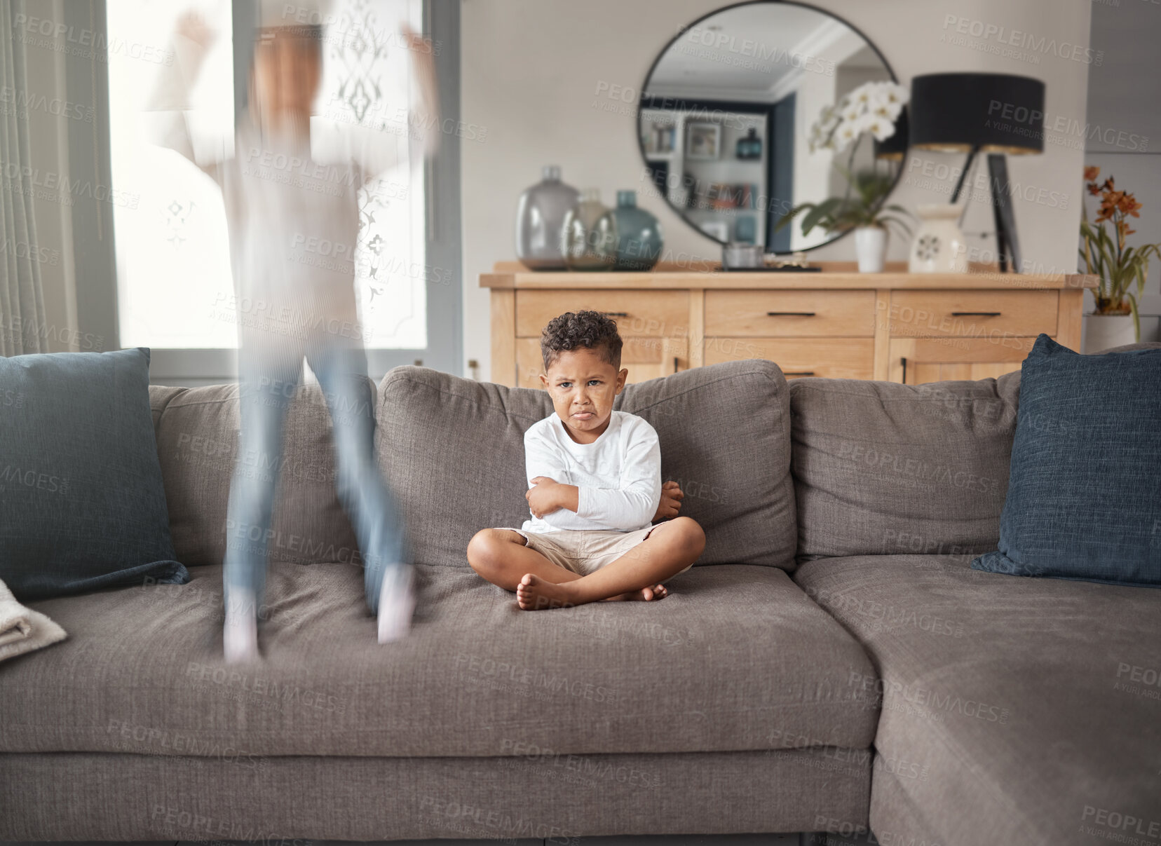 Buy stock photo Two young mixed race siblings showing their different personalities while sitting on a sofa at home. Cute child looking annoyed with his ADD sister