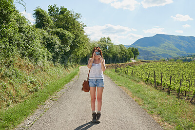 Woman traveling alone taking photos using her digital camera while standing in the road. Young woman on holiday alone taking photos with her digital camera next to a vineyard in the countryside
