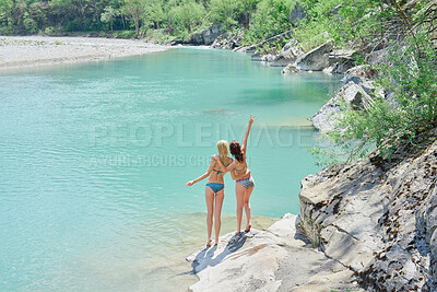 Woman in bikini making peace sign with arm around friend after swimming in the lake. Woman making the peace sign and celebrating after swimming in a lake with her friend on holiday.