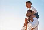 Young african american father carrying  his son on his shoulders against a blue sky while walking outdoors on a sunny day. Excited little boy having fun with his dad and enjoying summer vacation