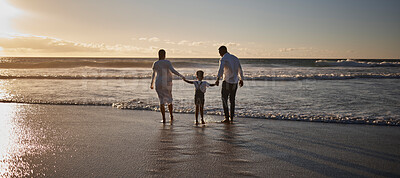 Rear view of a young african american family with one child getting their feet wet and having fun while spending time together by the beach at sunset