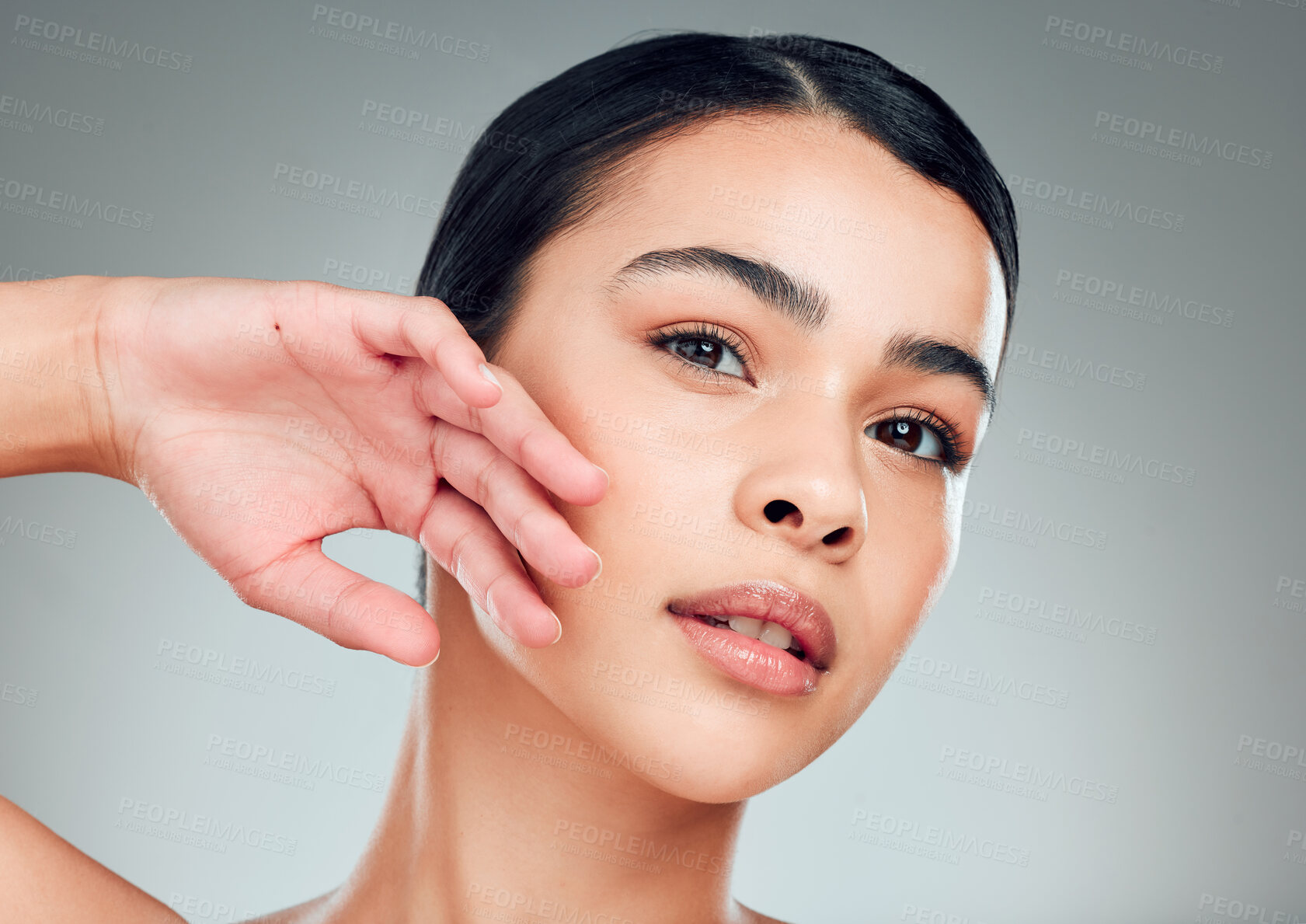 Buy stock photo Portrait of a beautiful mixed race woman touching smooth soft skin in a studio. Hispanic model with healthy natural glowing skin looking confident against grey copyspace while doing routine skincare