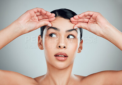 Buy stock photo One mixed race model feeling her face and looking worried about sagging skin. Hispanic woman thinking about getting botox against grey copyspace