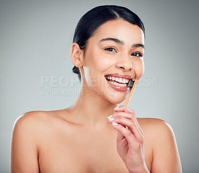 Studio portrait of a smiling mixed race young woman with glowing skin posing against grey copyspace background while brushing her teeth for fresh breath. Hispanic model using toothpaste to prevent a cavity