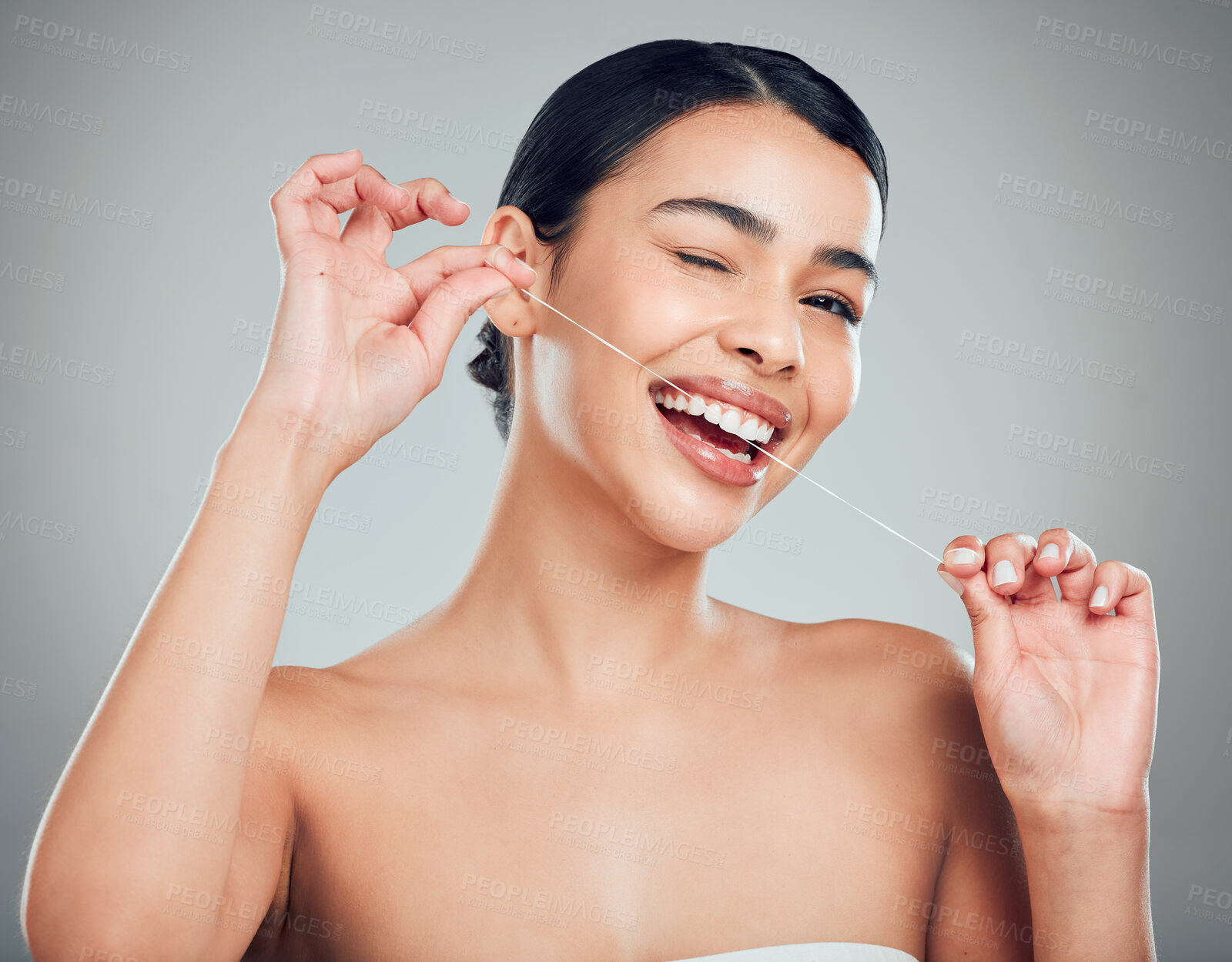 Buy stock photo Studio portrait of a smiling mixed race young woman with glowing skin posing against grey copyspace background while flossing her teeth for fresh breath. Hispanic model using floss to prevent a cavity