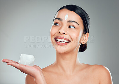 Buy stock photo A beautiful smiling mixed race woman applying cream to her face. Hispanic model with glowing skin holding moisturiser against a grey copyspace background