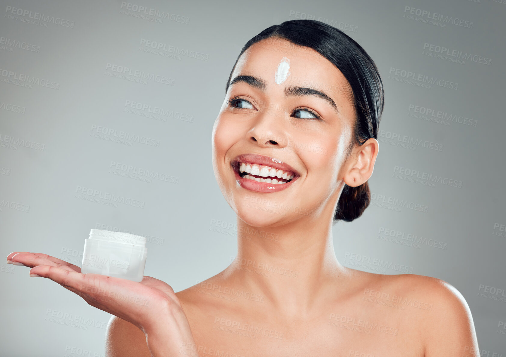Buy stock photo A beautiful smiling mixed race woman applying cream to her face. Hispanic model with glowing skin holding moisturiser against a grey copyspace background