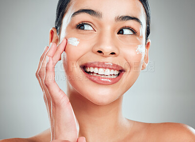 A beautiful smiling happy mixed race woman applying cream to her face. Hispanic model with glowing skin against a grey copyspace background