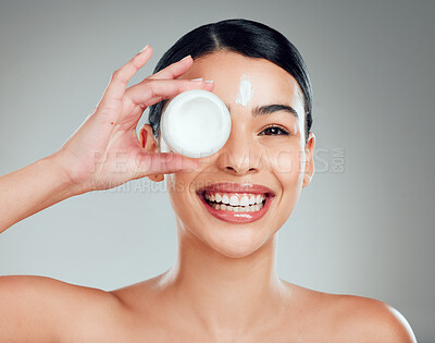 Studio Portrait of a beautiful smiling mixed race woman applying cream to her face. Hispanic model with glowing skin holding moisturiser against a grey copyspace background