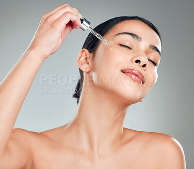 Buy stock photo A beautiful mixed race woman applying a soothing face serum to her radiant smooth face while posing against a blue background. Hispanic woman with flawless skin using essential oil