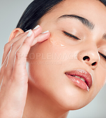 Buy stock photo A beautiful mixed race woman applying a soothing face serum to her radiant smooth face while posing against a blue background. Hispanic woman with flawless skin using essential oil