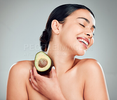 A happy mixed race woman holding an avocado. Hispanic model smiling and promoting the skin benefits of a healthy diet against a grey copyspace background