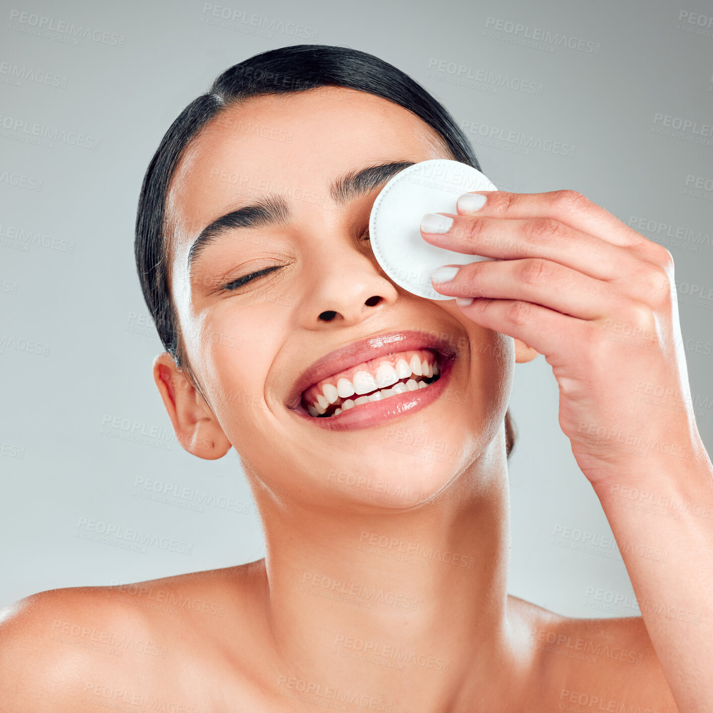 Buy stock photo A beautiful happy mixed race woman using a cotton pad to remove makeup during a grooming routine. Hispanic woman applying toner to her face against grey copyspace background in a studio