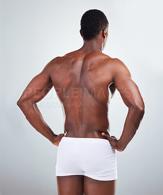 Rear view of one African American fitness model posing topless in a underwear and looking muscular. Black male athlete wearing boxers isolated on grey copyspace in a studio