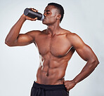 One young African American fitness model posing topless while drinking water from a bottle .Confident black male athlete isolated on grey copyspace is focused on staying hydrated while exercising